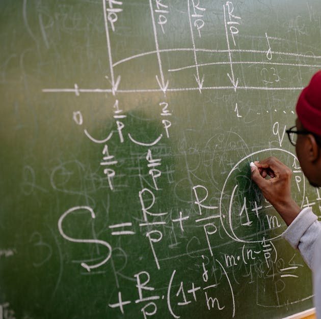 Student writing complex mathematical equations on a chalkboard in a classroom setting.