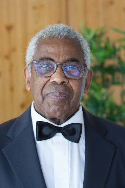Distinguished elderly man in a black suit and bowtie indoors, exuding elegance.